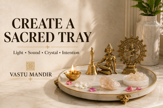 Sacred tray at home with diya, brass bell, crystal bowl, selenite plate, raw stone, and flowers arranged on a luxury marble surface.