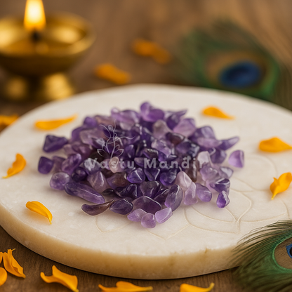Angled view of amethyst crystal chips on a white plate with marigold petals and a peacock feather