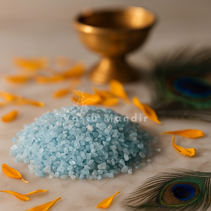 Angled view of aquamarine crystal chips on a white plate with marigold petals and a peacock feather