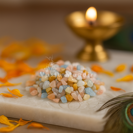 Multicoloured beryl crystal chips arranged on a carved white plate with marigold petals and a softly lit diya