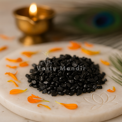 Black tourmaline crystal chips arranged on a carved white plate with marigold petals and a softly lit diya