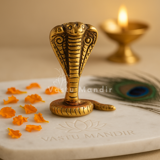 Three-headed brass snake idol on a sacred white plate with diya and marigold petals
