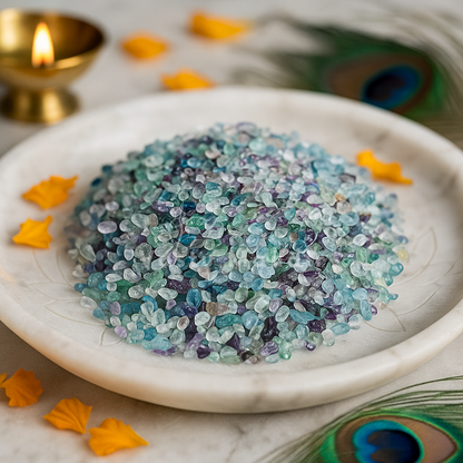 Fluorite crystal chips arranged on a carved white plate with marigold petals and a softly lit diya