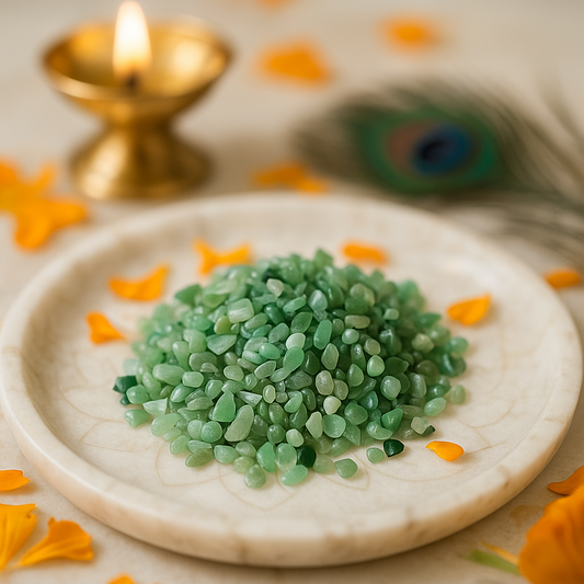Green aventurine crystal chips arranged on a carved white plate with marigold petals and a softly lit diya
