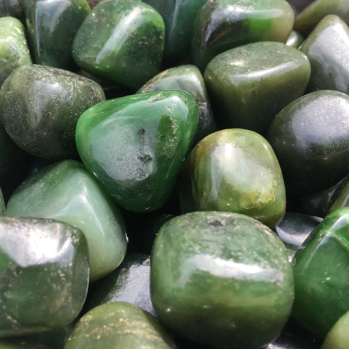 Macro close-up of dark green jade stones showing glossy surfaces and pale natural streaks