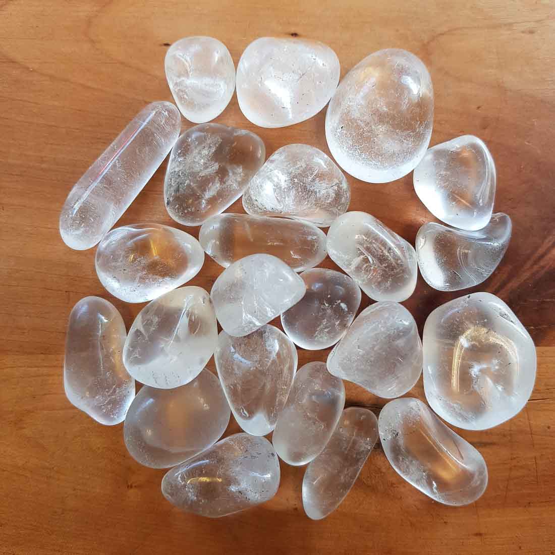 Clear quartz tumbled stones spread on a wooden surface in natural light