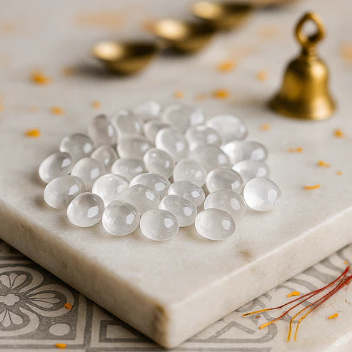 Angled view of clear quartz tumbled stones on a white plate with marigold petals and a peacock feather