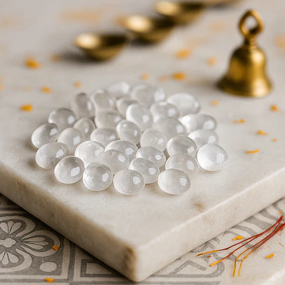 Angled view of clear quartz tumbled stones on a white plate with marigold petals and a peacock feather