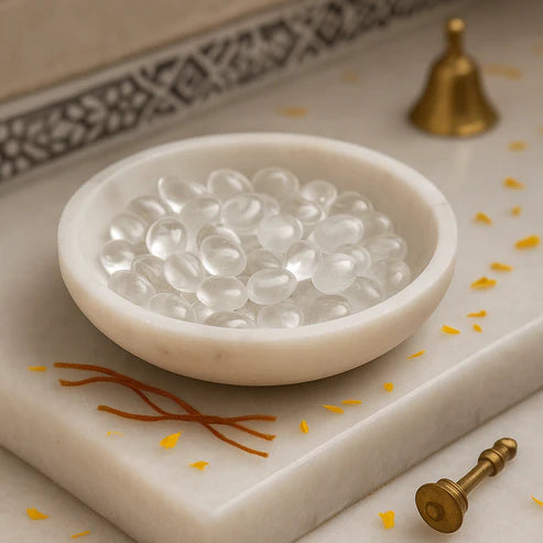 Clear quartz tumbled stones displayed in a white bowl beside a brass diya and pen