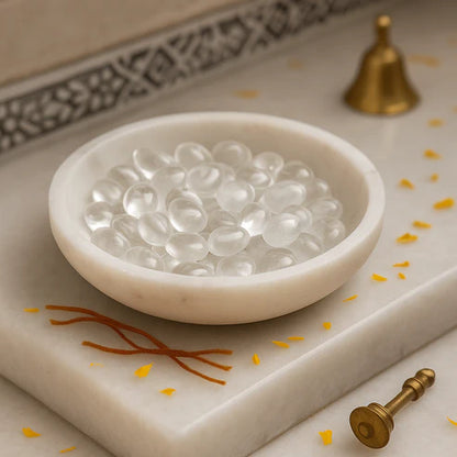 Clear quartz tumbled stones displayed in a white bowl beside a brass diya and pen