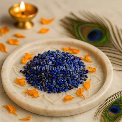Lapis lazuli crystal chips arranged on a carved white plate with marigold petals and a softly lit diya