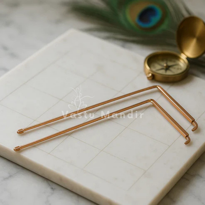 Angled copper L-rods arranged beside a compass and peacock feather