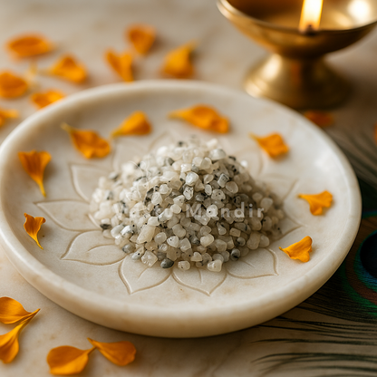 Angled view of moonstone crystal chips on a white plate with marigold petals and a peacock feather