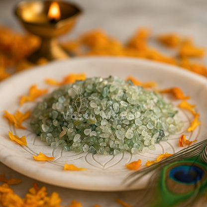 Angled view of prehnite crystal chips on a white plate with marigold petals and a peacock feather