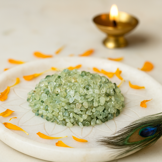 Prehnite crystal chips arranged on a carved white plate with marigold petals and a softly lit diya