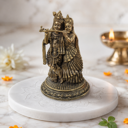 Brass Radha Krishna idol on a sacred white plate with diya and marigold petals