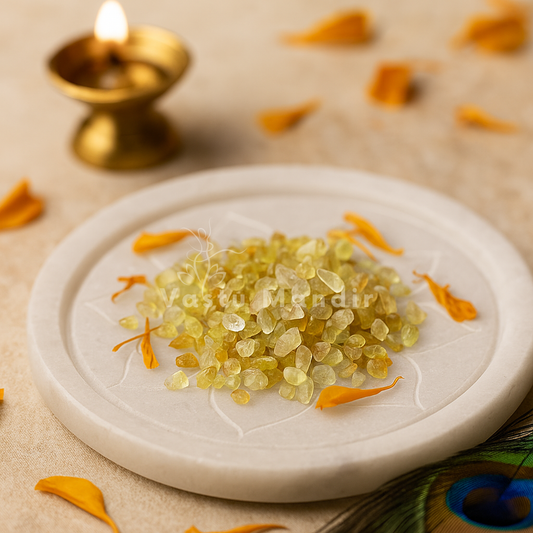 Yellow sapphire chips arranged on a white plate with marigold petals and a brass diya