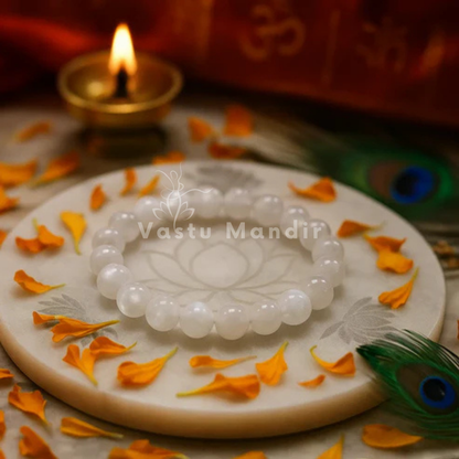 100% Natural Rainbow Moonstone (White) on a decorative plate with orange petals and a lit candle in the background, featuring 'Vastu Mandir' branding.