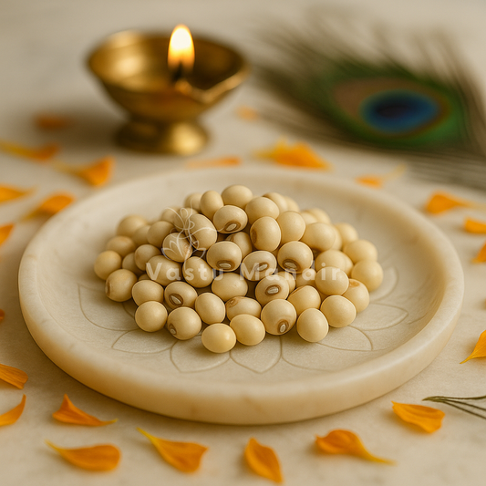 White gumchi seeds arranged on a white plate with marigold petals and a softly lit diya
