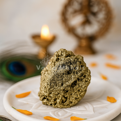 Rough metallic pyrite cluster displayed on a white plate with marigold petals and a diya