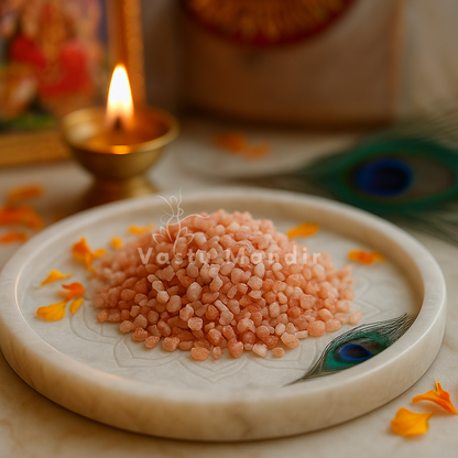 Raw sunstone chips on a white plate with a framed deity and softly lit diya behind them