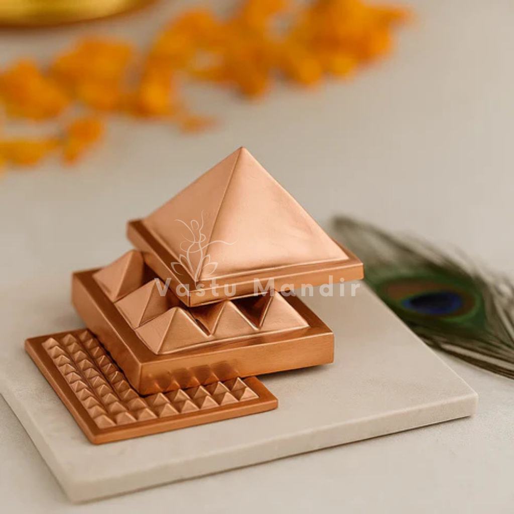 Three copper pyramid layers displayed stacked and offset on a white platform with marigold petals and a peacock feather