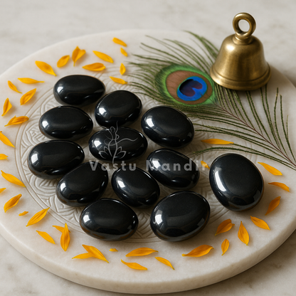 Hematite tumbled stones arranged on a carved white plate with marigold petals and a softly lit diya