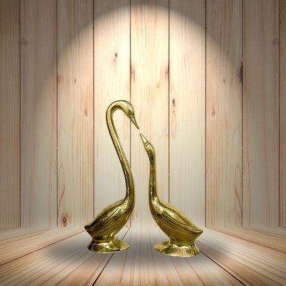 Brass swan pair displayed together in a softly lit wooden alcove