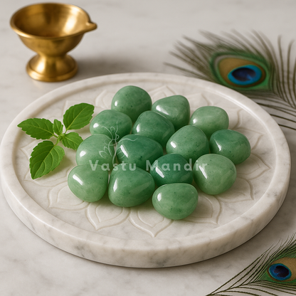 Angled view of green aventurine tumbled stones on a white plate with marigold petals and a peacock feather