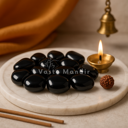 Angled view of black onyx tumbled stones on a white plate with marigold petals and a peacock feather