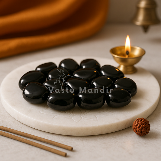Black onyx tumbled stones arranged on a carved white plate with marigold petals and a softly lit diya