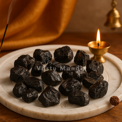 Rough black tourmaline stones arranged on a dark plate with a softly lit diya behind them