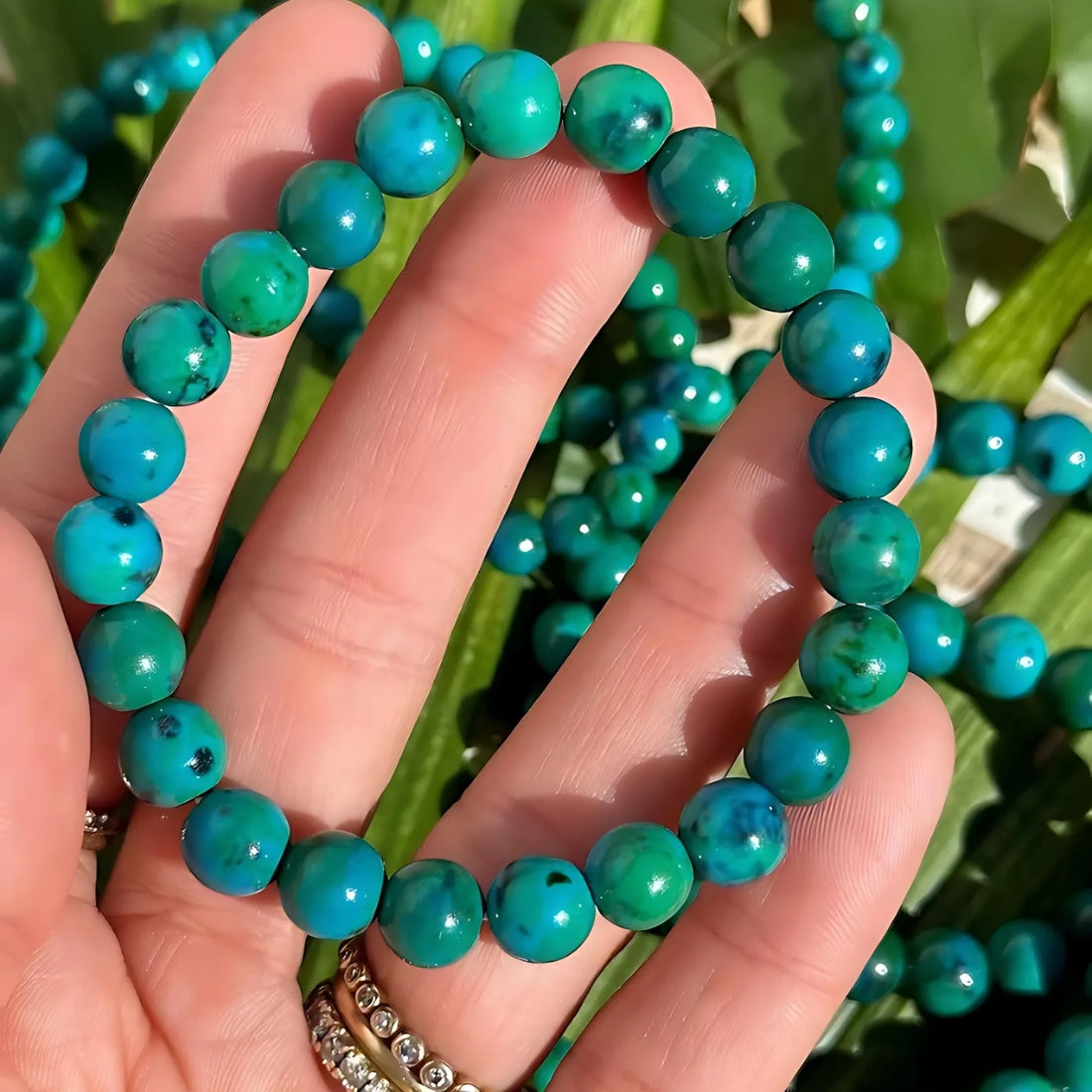 Multiple turquoise chrysocolla bead strands held against a hand