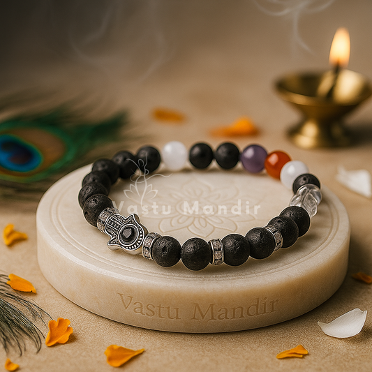 Black beaded bracelet with a silver Hamsa hand charm on a beige stone platter with 'Vastu Mandir' branding.
