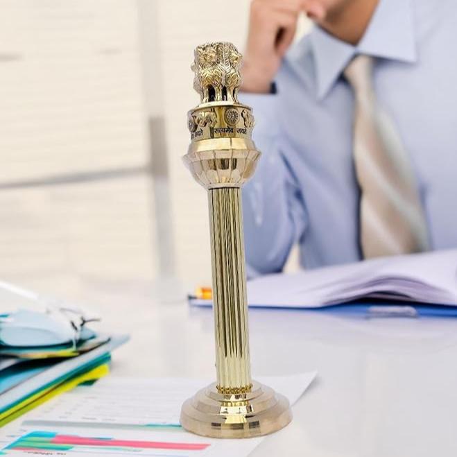 Brass Ashoka Pillar idol displayed on a study desk beside a seated professional