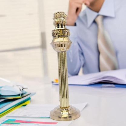 Brass Ashoka Pillar idol displayed on a study desk beside a seated professional