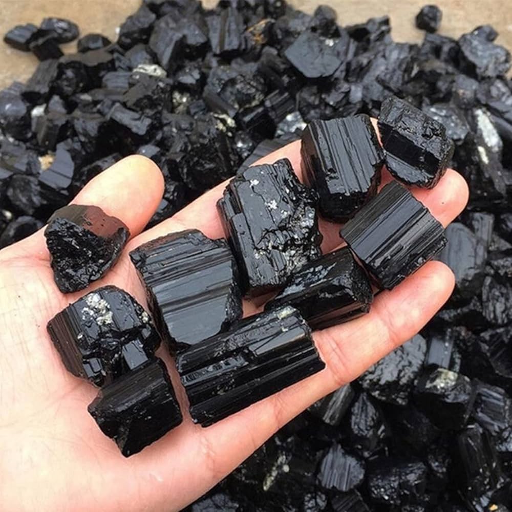 Hand holding mixed black tourmaline rods and rough chunks for a close product view
