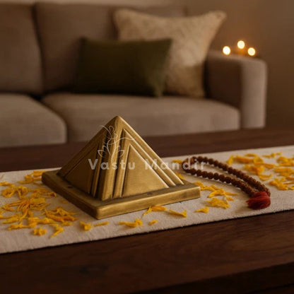 Two-layer brass Vastu pyramid displayed on a living-room coffee table with marigold petals and a Rudraksha mala