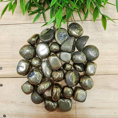 Pyrite tumbled stones spread on a wooden surface in natural light