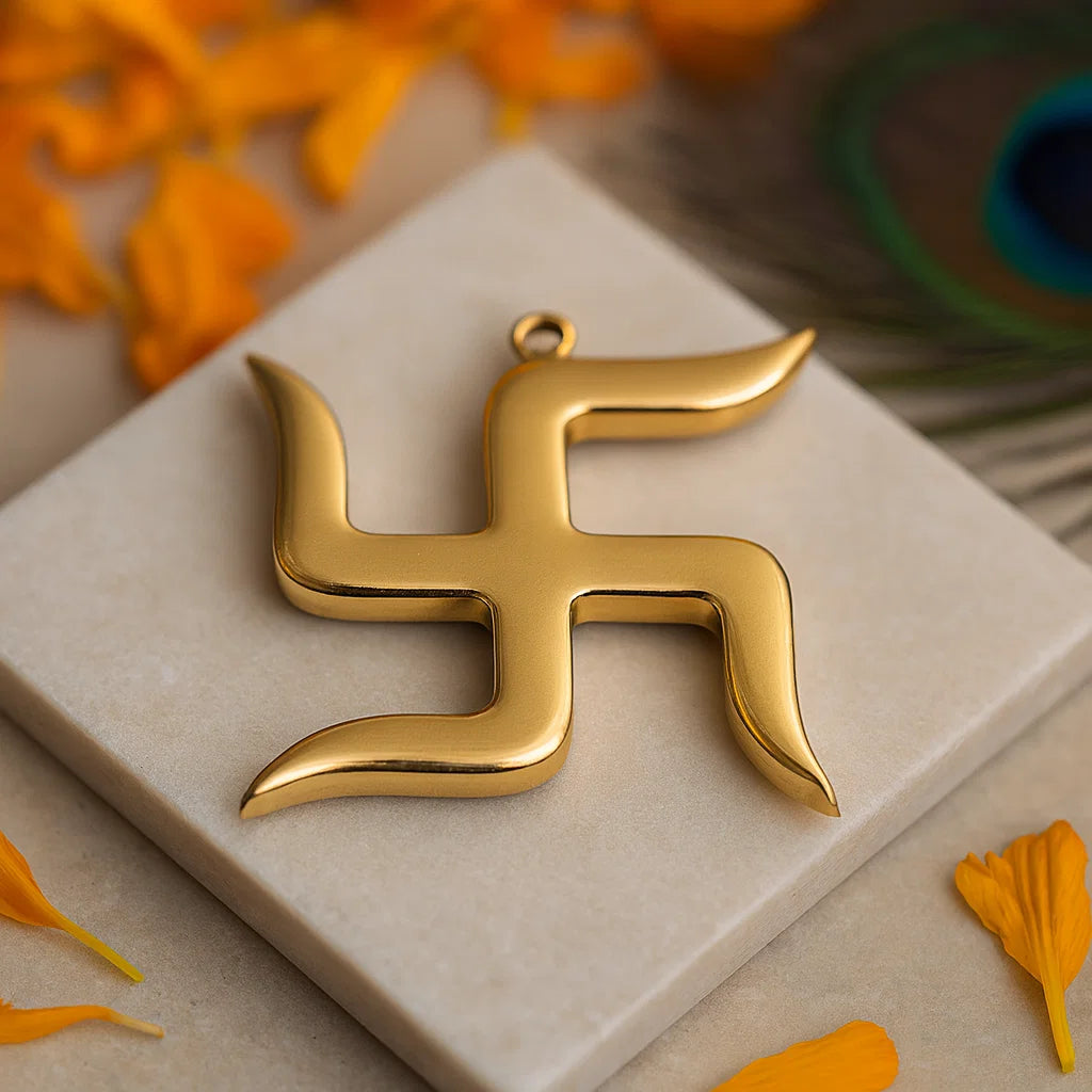 Brass swastik symbol  on a beige surface with orange flowers and a peacock feather in the background