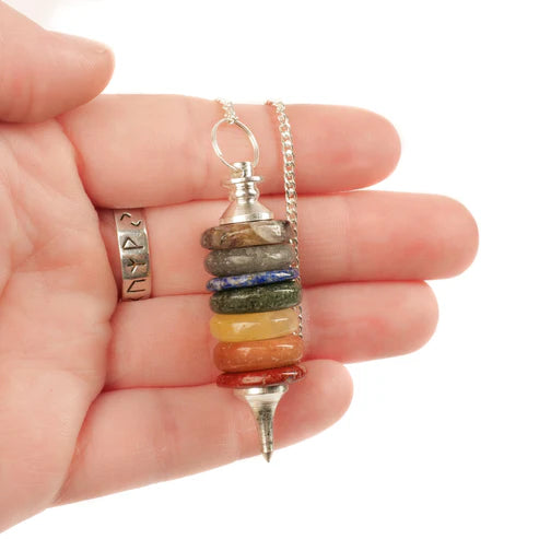 Seven chakra pendulum held in hand with silver chain and ring for scale