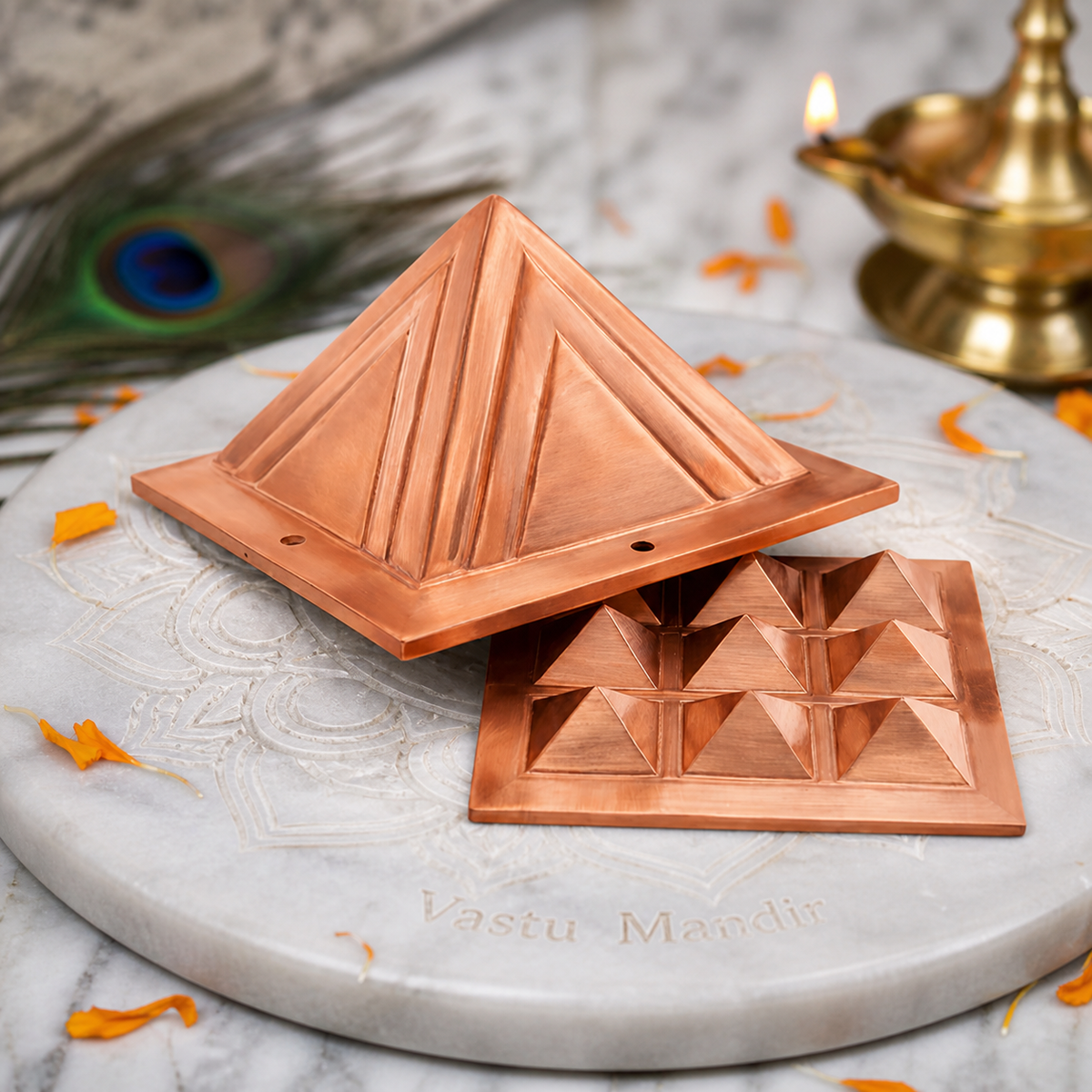 Two copper pyramid layers displayed separately on a carved marble plate with marigold petals and a brass diya