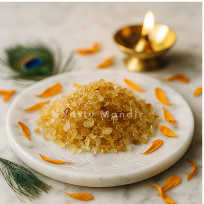 Angled view of citrine crystal chips on a white plate with marigold petals and a peacock feather