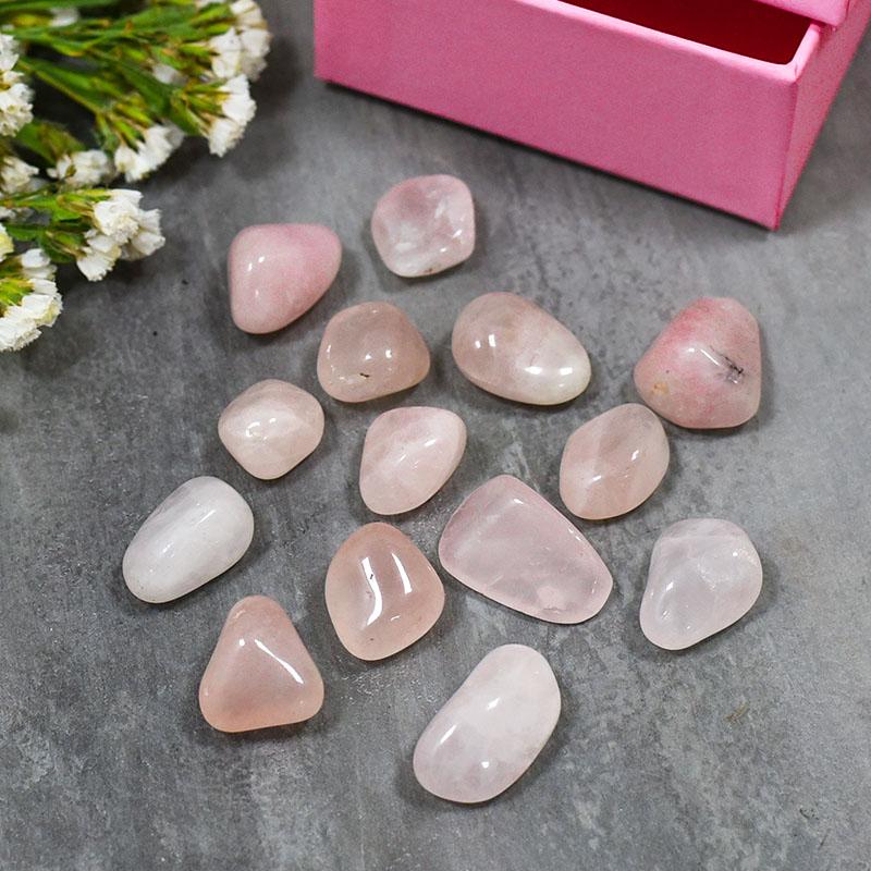Rose quartz tumbled stones spread on a wooden surface in natural light