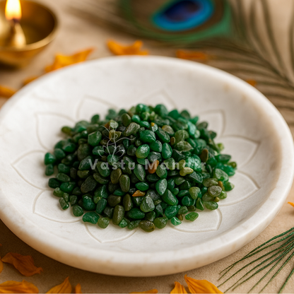 Angled view of emerald crystal chips on a white plate with marigold petals and a peacock feather