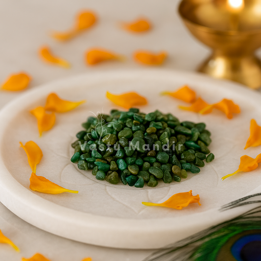 Emerald crystal chips arranged on a carved white plate with marigold petals and a softly lit diya