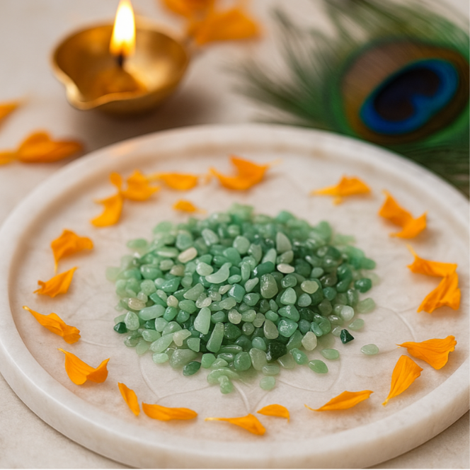 Angled view of green aventurine crystal chips on a white plate with marigold petals and a peacock feather