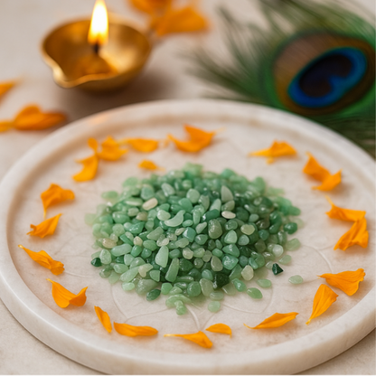 Angled view of green aventurine crystal chips on a white plate with marigold petals and a peacock feather