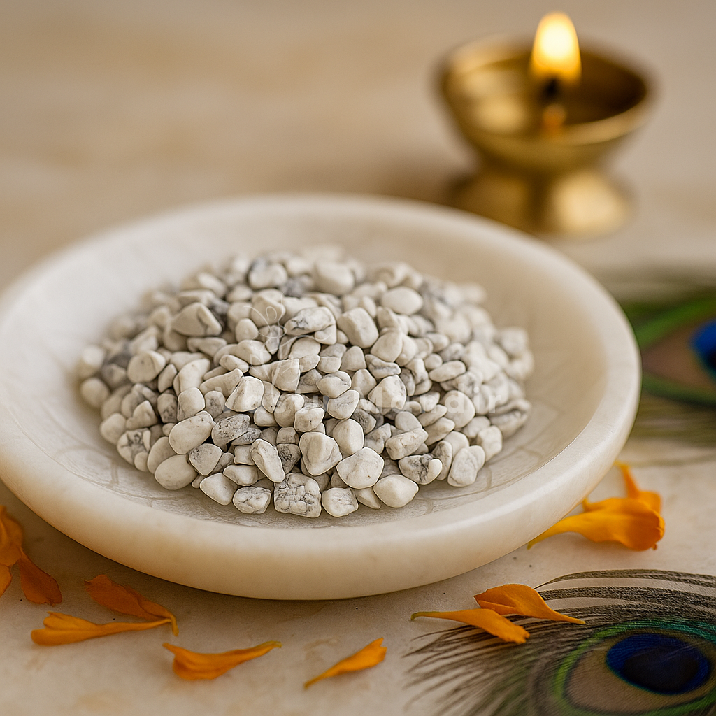 Howlite crystal chips arranged on a carved white plate with marigold petals and a softly lit diya