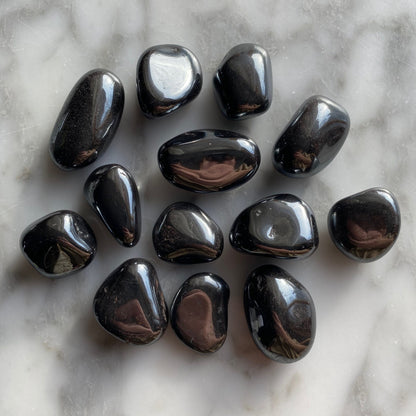 Hematite tumbled stones spread on a wooden surface in natural light